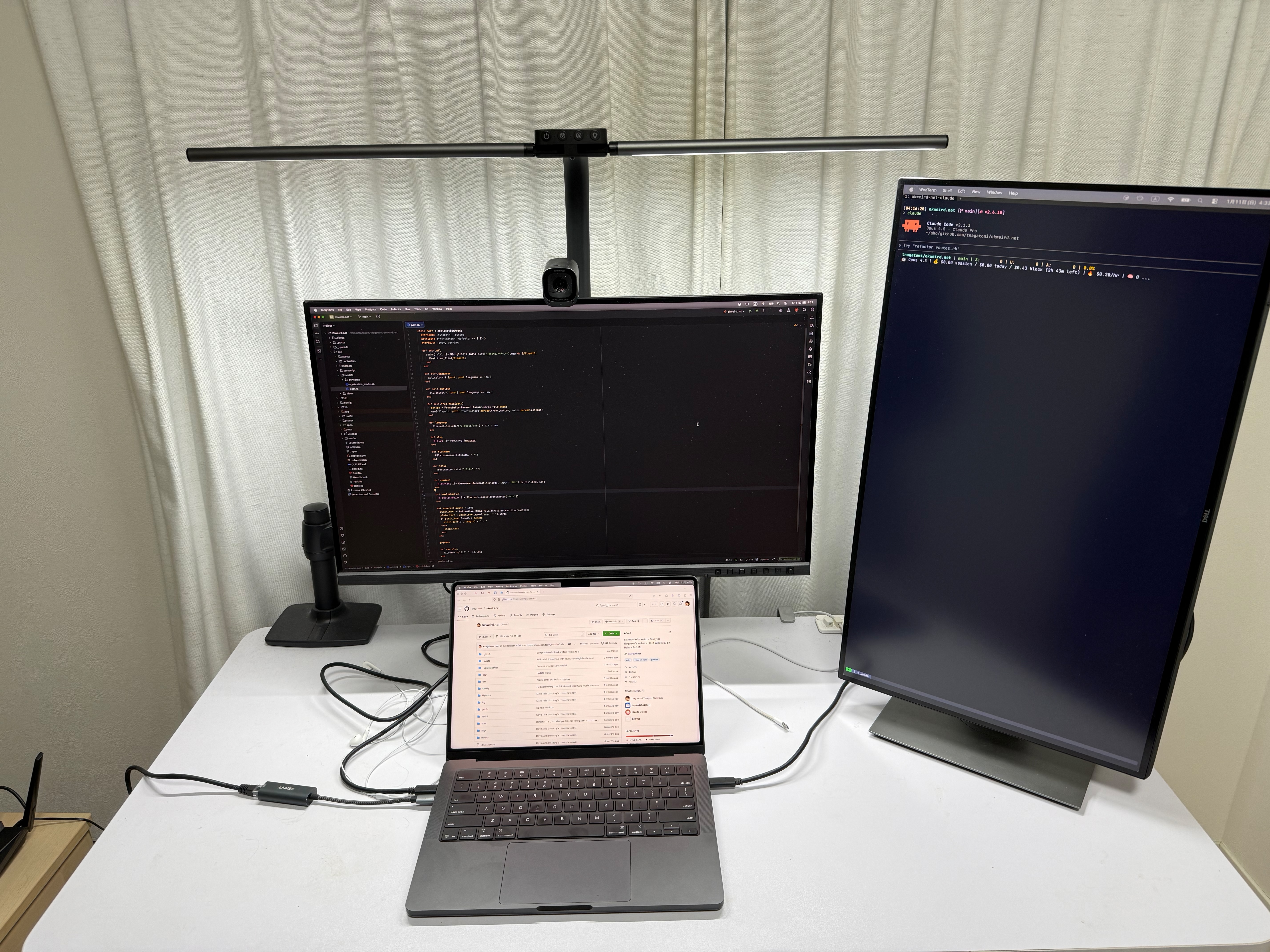 デスク環境。中央にMacBook 1台の上に横置きモニター、右に立て置きモニターが並んでいる。